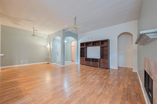 30606 S Sulphur Creek Dr, Magnolia, TX 77355 - unfurnished living room featuring a ceiling fan, arched walkways, light wood-style floors, a fireplace, and a textured ceiling