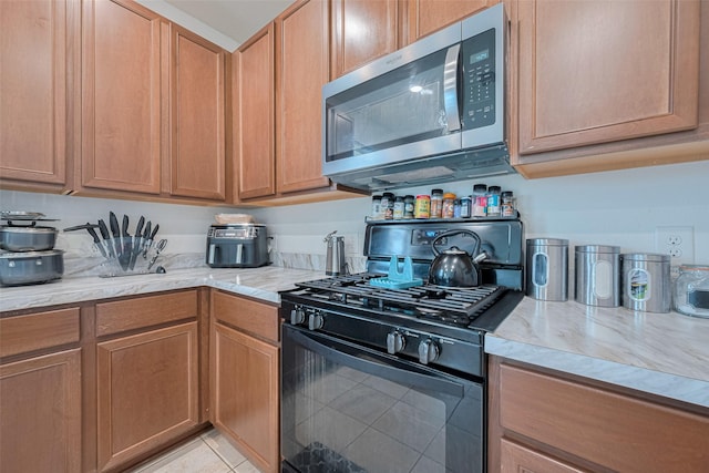602 Willow Briar Dr, Houston, TX 77090 - kitchen featuring black gas range oven, stainless steel microwave, light stone counters, and light tile patterned flooring