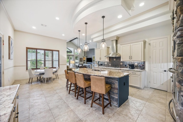 5214 Bristol Bank Ct, Houston, TX 77041 - kitchen featuring wall chimney exhaust hood, backsplash, light stone counters, a breakfast bar area, and a kitchen island with sink