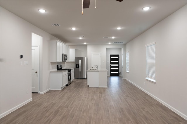 64 Valiant Ridge Trl, Magnolia, TX 77354 - kitchen with stainless steel appliances, ceiling fan, light wood-style flooring, an island with sink, and white cabinetry
