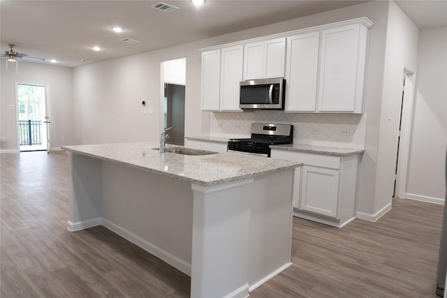 64 Valiant Ridge Trl, Magnolia, TX 77354 - kitchen with appliances with stainless steel finishes, wood finished floors, decorative backsplash, a kitchen island with sink, and white cabinetry