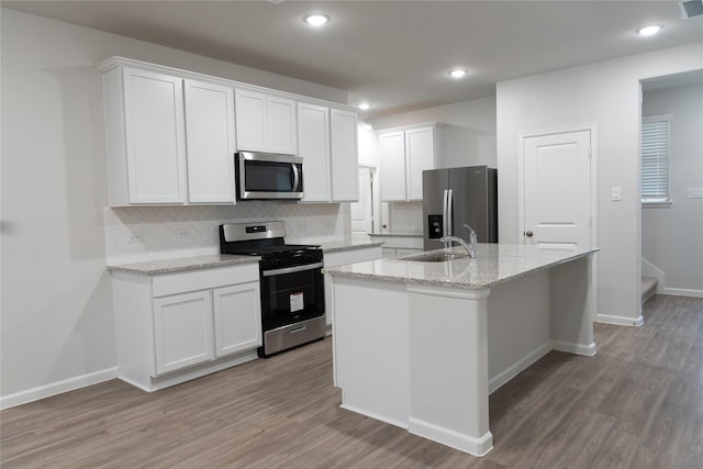 64 Valiant Ridge Trl, Magnolia, TX 77354 - kitchen with stainless steel appliances, an island with sink, backsplash, light wood finished floors, and recessed lighting