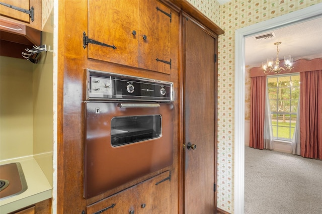2718 Stratford St, Pearland, TX 77581 - kitchen featuring oven, wallpapered walls, a chandelier, brown cabinetry, and carpet