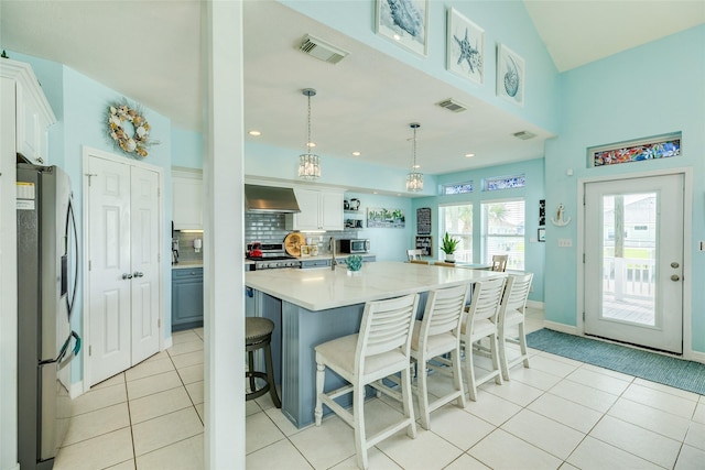 18614 Warrior Rd, Galveston, TX 77554 - kitchen with stainless steel appliances, wall chimney exhaust hood, a breakfast bar area, white cabinetry, and light tile patterned floors