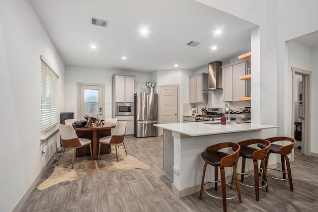 12810 Barnesbury Ln, Houston, TX 77047 - kitchen with appliances with stainless steel finishes, wall chimney exhaust hood, a peninsula, light wood-type flooring, and a kitchen bar