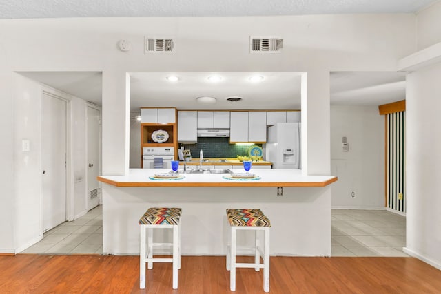 1202 Fay Rd, Kemah, TX 77565 - kitchen featuring white appliances, light tile patterned floors, under cabinet range hood, and a breakfast bar area