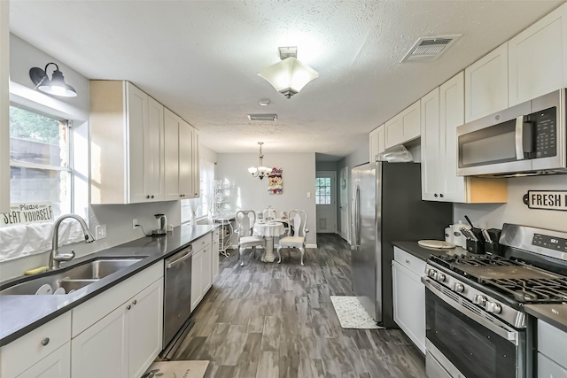 637 Mosswood Dr, Conroe, TX 77302 - kitchen with appliances with stainless steel finishes, dark countertops, a chandelier, white cabinets, and a textured ceiling