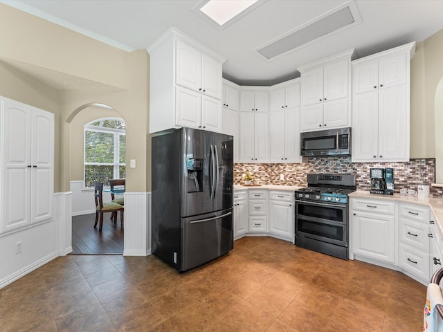 3139 Prairiestone Trail Ln, Katy, TX 77450 - kitchen featuring stainless steel appliances, arched walkways, white cabinetry, a wainscoted wall, and backsplash