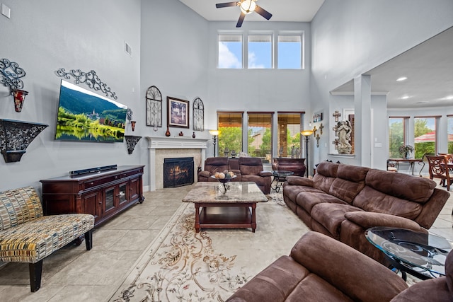 207 Fox Squirrel Ct, Pinehurst, TX 77362 - living room featuring a high ceiling, ceiling fan, healthy amount of natural light, a lit fireplace, and light stone finish floors