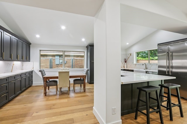 4543 Warm Springs Rd, Houston, TX 77035 - kitchen featuring built in fridge, vaulted ceiling, tasteful backsplash, a kitchen breakfast bar, and light wood-style floors
