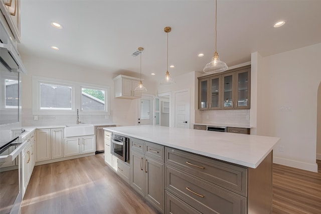 1026 W Cottage St, Houston, TX 77009 - kitchen with light wood-style floors, decorative backsplash, stainless steel oven, glass insert cabinets, and light countertops