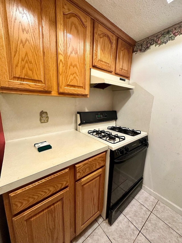 6206 Antha St, Houston, TX 77016 - kitchen with under cabinet range hood, range with gas cooktop, light tile patterned flooring, light countertops, and brown cabinets