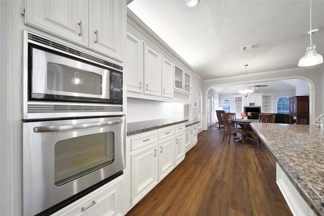 2206 Hickory Park Dr, Kingwood, TX 77345 - kitchen featuring stainless steel appliances, arched walkways, dark wood-style flooring, a textured ceiling, and white cabinetry