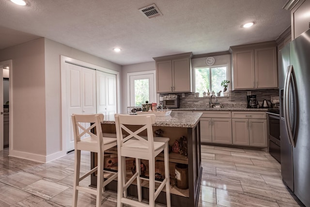 26752 Diamond Sq, Splendora, TX 77372 - kitchen with stainless steel fridge with ice dispenser, gray cabinets, light stone countertops, backsplash, and a center island