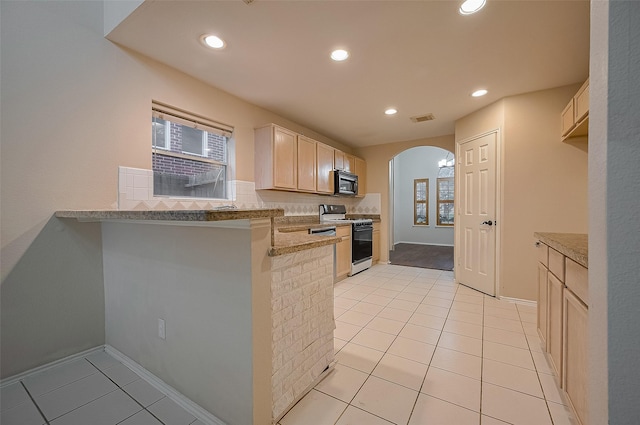 23035 Canal Rd, Richmond, TX 77406 - kitchen with white gas range oven, black microwave, arched walkways, light tile patterned floors, and tasteful backsplash