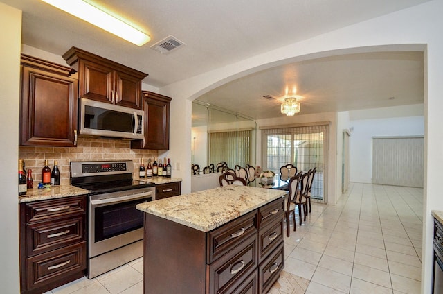 10723 Bexley Dr, Houston, TX 77099 - kitchen featuring stainless steel appliances, light tile patterned flooring, decorative backsplash, arched walkways, and light stone countertops