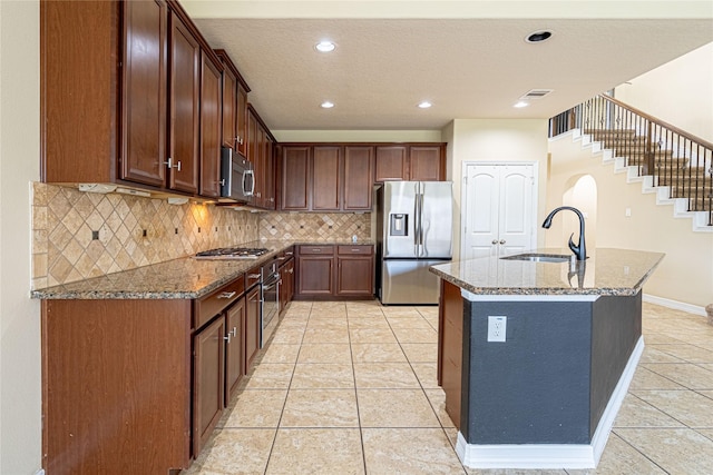 22411 Limestone Crest Ln, Katy, TX 77449 - kitchen with appliances with stainless steel finishes, light tile patterned floors, dark stone counters, backsplash, and a kitchen island with sink
