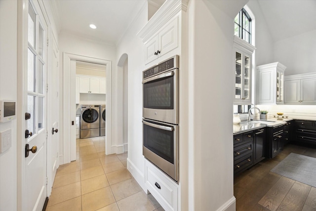 10825 Smithdale Rd, Houston, TX 77024 - kitchen featuring stainless steel double oven, independent washer and dryer, white cabinetry, dark cabinets, and glass insert cabinets
