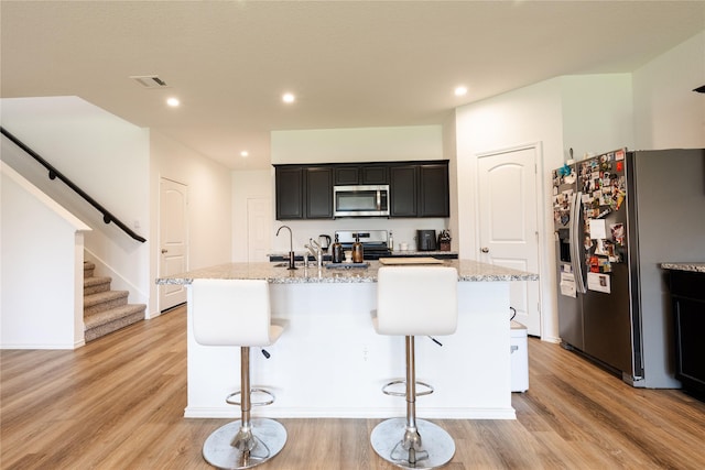 21427 Hawthorn Prairie Dr, New Caney, TX 77357 - kitchen with appliances with stainless steel finishes, light wood finished floors, a breakfast bar area, a kitchen island with sink, and light stone countertops