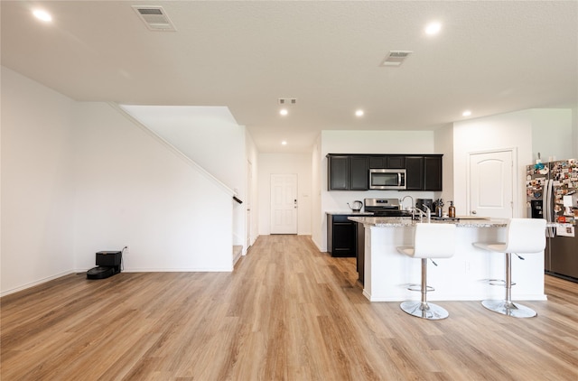 21427 Hawthorn Prairie Dr, New Caney, TX 77357 - kitchen featuring appliances with stainless steel finishes, a kitchen island with sink, light wood finished floors, recessed lighting, and dark cabinets