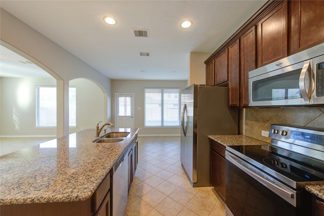 8115 Heartbrook Field Ln, Cypress, TX 77433 - kitchen featuring stainless steel appliances, arched walkways, light stone counters, tasteful backsplash, and light tile patterned floors