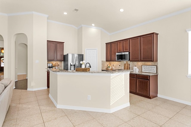 26642 Becker Pines Ln, Katy, TX 77494 - kitchen with appliances with stainless steel finishes, light tile patterned floors, tasteful backsplash, arched walkways, and a center island with sink