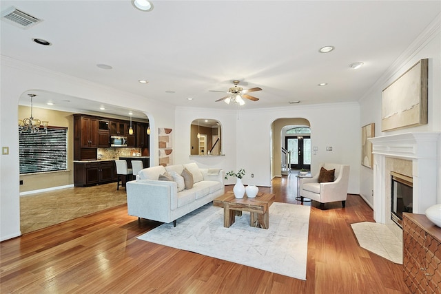 1423 Meadow Lakes Dr, Sugar Land, TX 77479 - living area with arched walkways, light wood-style flooring, a ceiling fan, a tiled fireplace, and ornamental molding