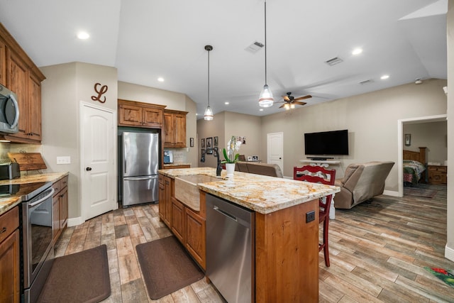 6112 Guyler St, Wallis, TX 77485 - kitchen with stainless steel appliances, brown cabinets, light wood-style floors, light stone counters, and a ceiling fan