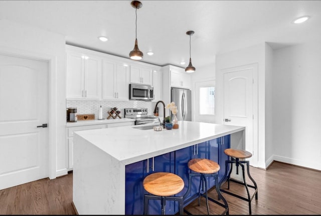 3021 Prospect St, Houston, TX 77004 - kitchen featuring appliances with stainless steel finishes, white cabinetry, a center island with sink, decorative light fixtures, and a kitchen breakfast bar