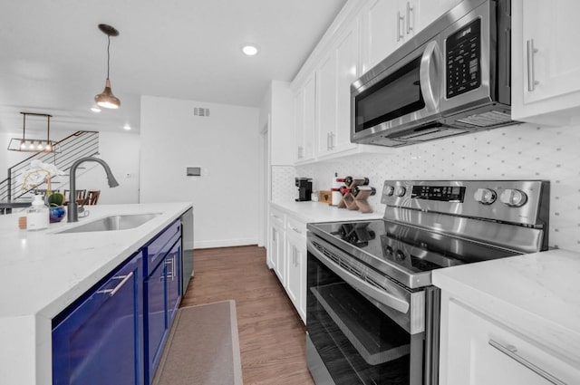 3021 Prospect St, Houston, TX 77004 - kitchen featuring appliances with stainless steel finishes, blue cabinetry, white cabinetry, wood finished floors, and recessed lighting