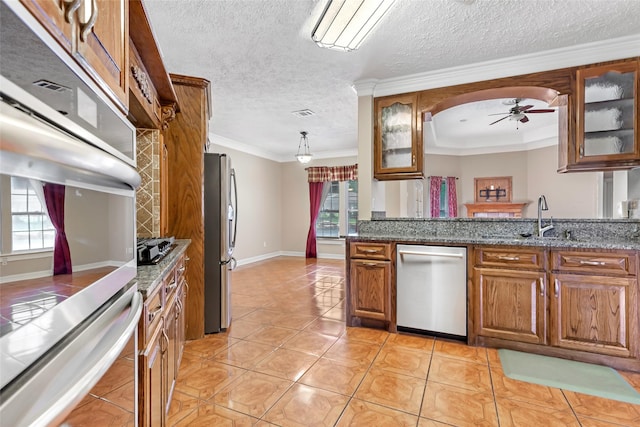 15908 Mcnorton, Splendora, TX 77372 - kitchen featuring appliances with stainless steel finishes, brown cabinets, a ceiling fan, glass insert cabinets, and a textured ceiling