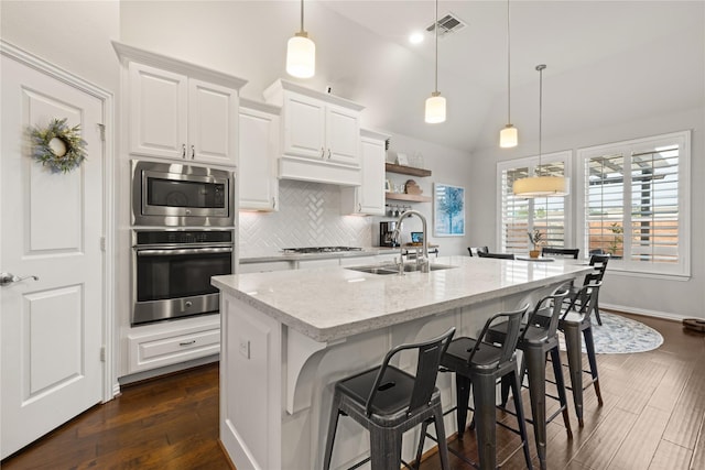 8903 Purdy Crescent Trl, Richmond, TX 77406 - kitchen with appliances with stainless steel finishes, dark wood-style flooring, tasteful backsplash, white cabinetry, and a center island with sink