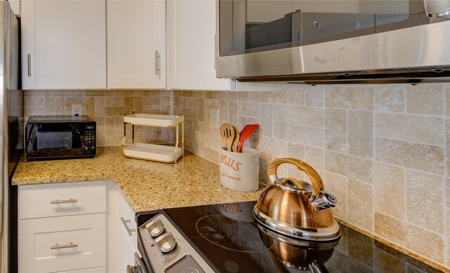 8100 Cambridge St Unit 114, Houston, TX 77054 - kitchen with stainless steel microwave, black microwave, white cabinetry, decorative backsplash, and light stone countertops