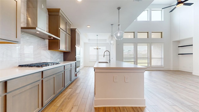 23604 Olive Creek Ln, New Caney, TX 77357 - kitchen featuring wall chimney exhaust hood, appliances with stainless steel finishes, light wood-style floors, light countertops, and an island with sink