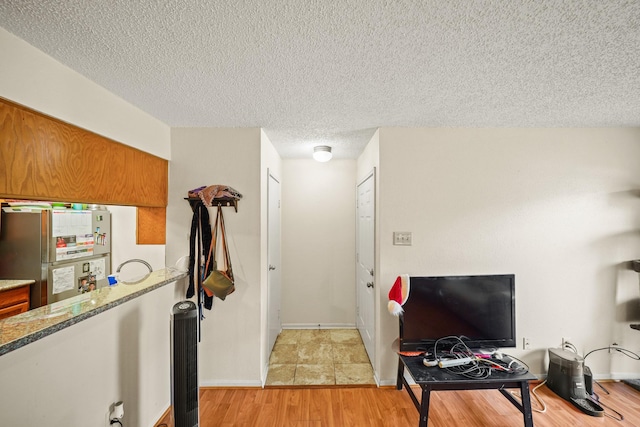 2120 El Paseo St Unit 1403, Houston, TX 77054 - kitchen with freestanding refrigerator, a textured ceiling, brown cabinetry, light wood finished floors, and stone counters