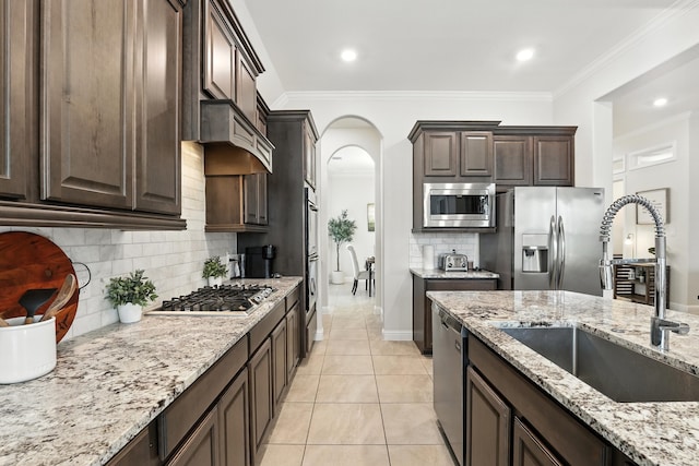 15415 Wildpoint Dr, Cypress, TX 77429 - kitchen featuring stainless steel appliances, arched walkways, dark brown cabinetry, light stone counters, and tasteful backsplash