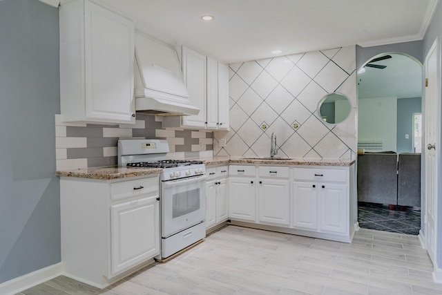4218 E Terrace Creek Cir, Houston, TX 77014 - kitchen with white range with gas cooktop, custom exhaust hood, backsplash, white cabinets, and crown molding