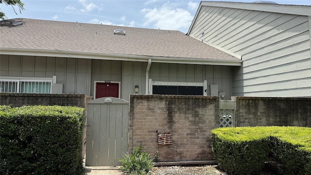 12922 Wirevine Ln, Houston, TX 77072 - view of exterior entry with board and batten siding, a shingled roof, and a gate
