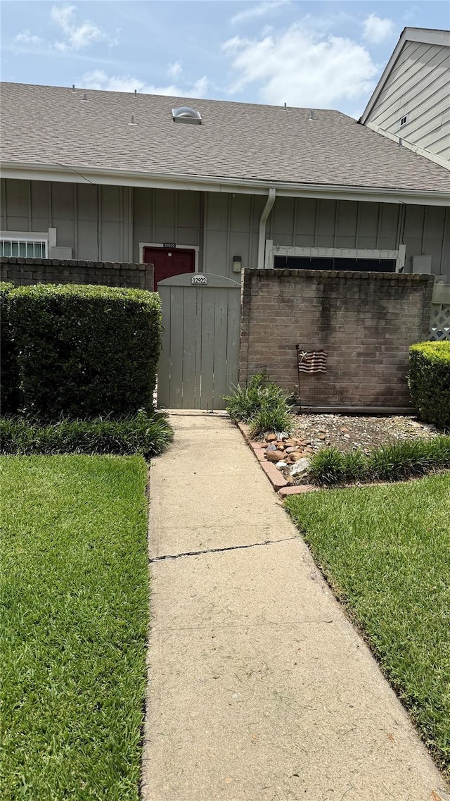 12922 Wirevine Ln, Houston, TX 77072 - view of exterior entry featuring board and batten siding, a shingled roof, brick siding, and a lawn