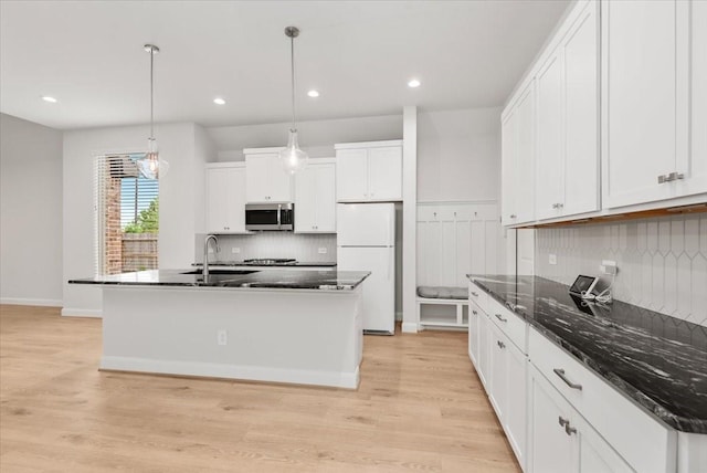 12831 Raemoir Dr, Humble, TX 77346 - kitchen with stainless steel microwave, freestanding refrigerator, decorative backsplash, light wood-type flooring, and white cabinets