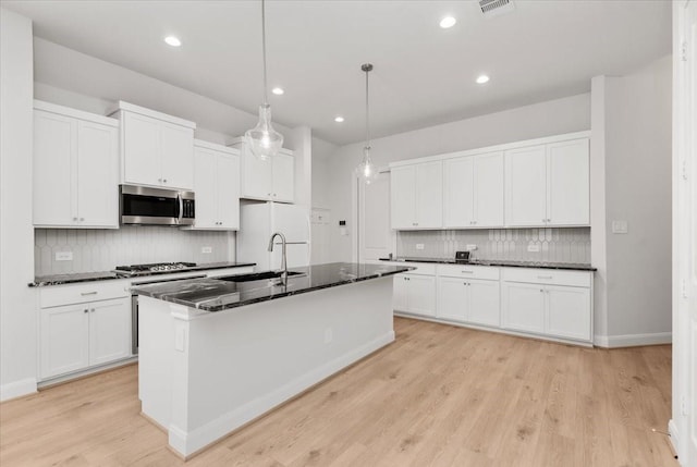 12831 Raemoir Dr, Humble, TX 77346 - kitchen with stainless steel appliances, backsplash, an island with sink, light wood-type flooring, and white cabinets