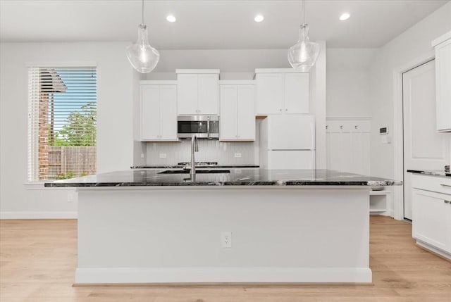 12831 Raemoir Dr, Humble, TX 77346 - kitchen with stainless steel microwave, freestanding refrigerator, an island with sink, white cabinetry, and dark stone counters