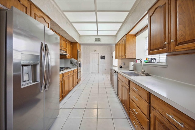 2701 11th St N, Texas City, TX 77590 - kitchen with appliances with stainless steel finishes, light tile patterned floors, light countertops, under cabinet range hood, and brown cabinets