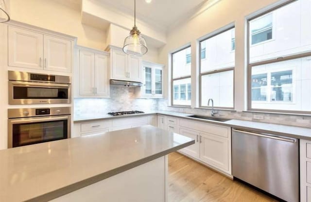 4041 Leeland St, Houston, TX 77023 - kitchen featuring appliances with stainless steel finishes, white cabinets, light wood finished floors, and decorative backsplash