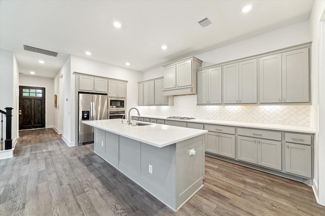 16630 Polletts Cove Ct, Humble, TX 77346 - kitchen featuring stainless steel appliances, gray cabinets, decorative backsplash, a kitchen island with sink, and wood finished floors