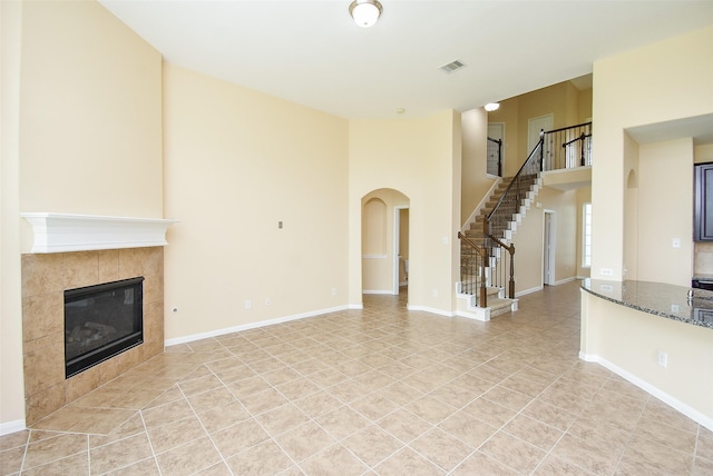 20315 Cypress Poll Dr, Cypress, TX 77433 - unfurnished living room with a high ceiling, stairway, a tiled fireplace, light tile patterned floors, and arched walkways
