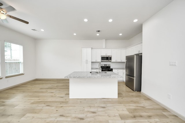 2119 Esther Dr, Houston, TX 77088 - kitchen featuring appliances with stainless steel finishes, ceiling fan, white cabinetry, a kitchen island with sink, and tasteful backsplash