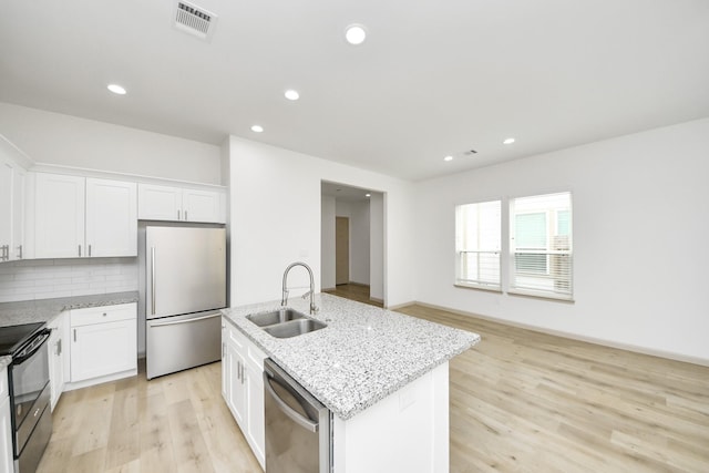 2119 Esther Dr, Houston, TX 77088 - kitchen featuring appliances with stainless steel finishes, light wood-style floors, light stone counters, a center island with sink, and decorative backsplash