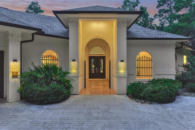 134 Trinity Oaks Ct, The Woodlands, TX 77381 - exterior entry at dusk with a high end roof, stucco siding, and french doors