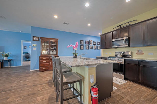 22618 Cremona Village Trl, Katy, TX 77449 - kitchen with appliances with stainless steel finishes, wood finished floors, a kitchen island with sink, a breakfast bar, and dark brown cabinets